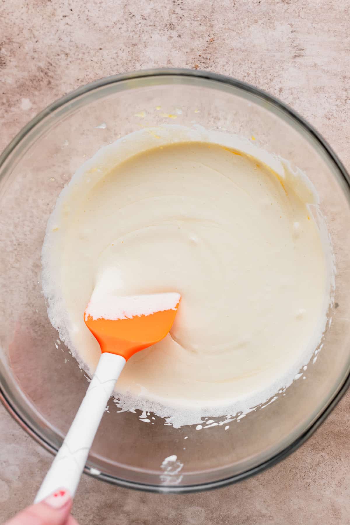 Whipped sugar and eggs in a glass bowl with a rubber spatula.