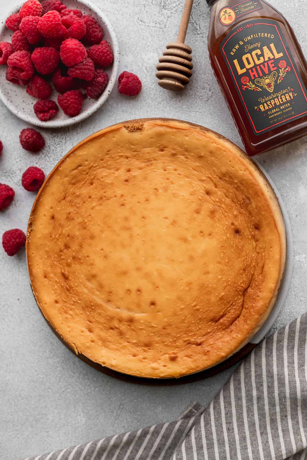 Baked cheesecake on a platter surrounded by raspberries.