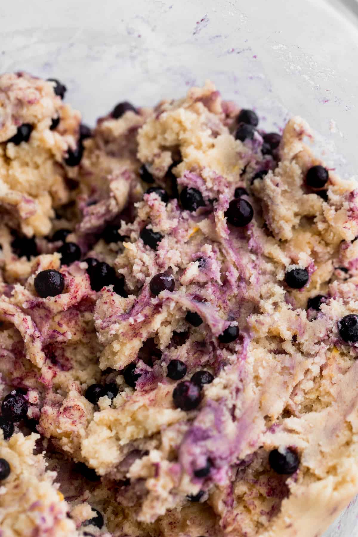 Blueberries swirled into cookie dough in a glass bowl.