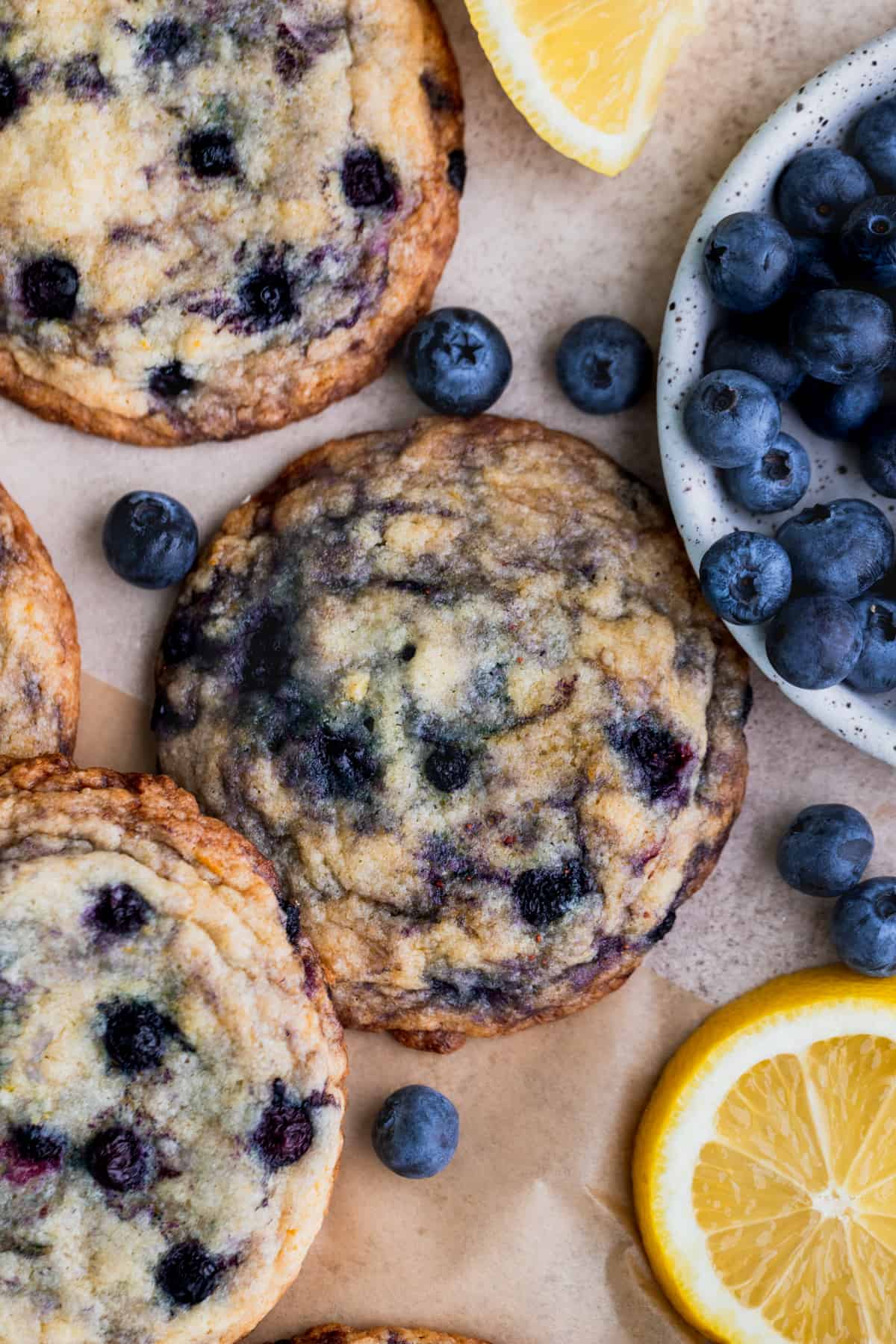 Three lemon blueberry cookies on parchment paper with fresh blueberries around it.