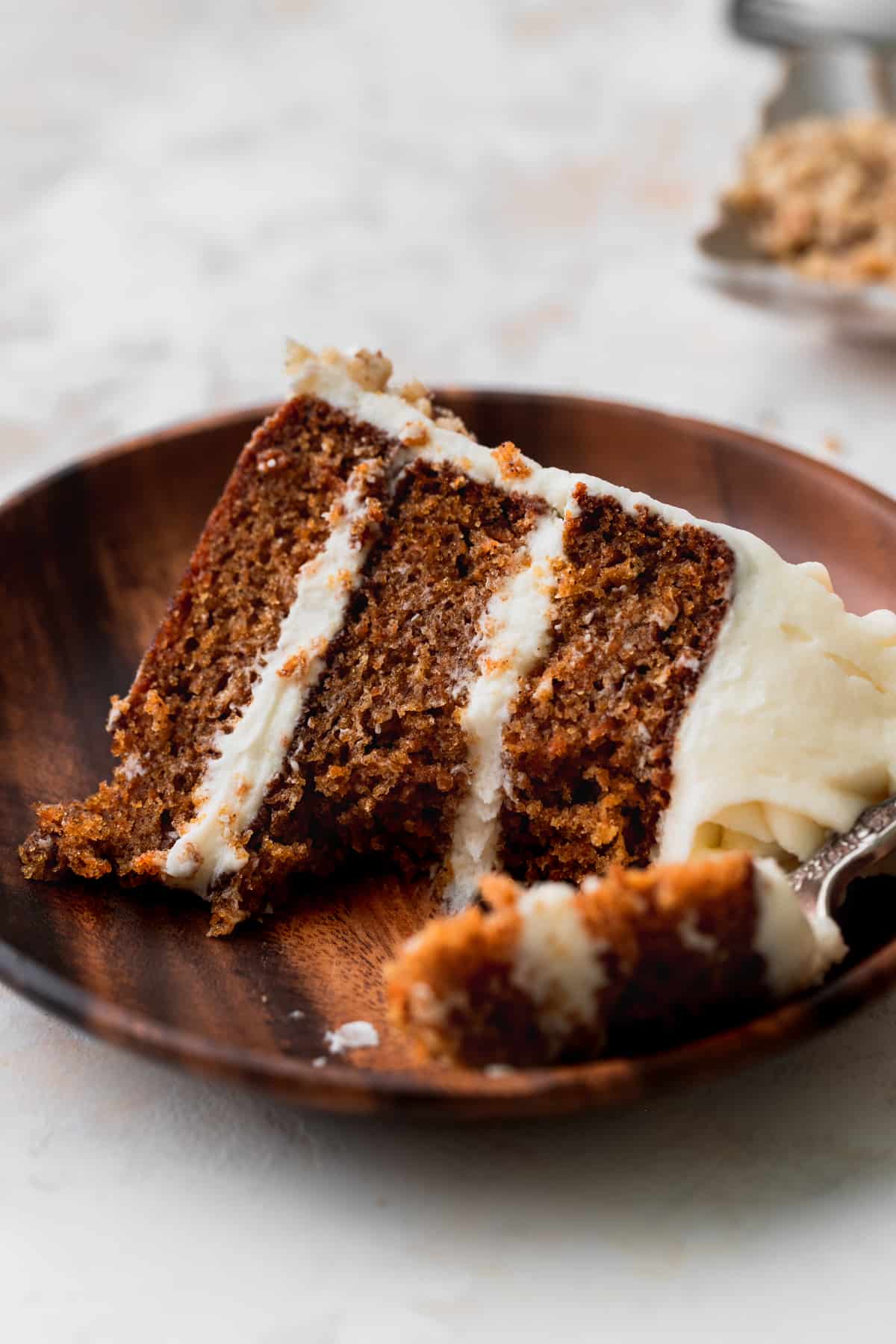 Slice of carrot cake on a plate with a bite missing.