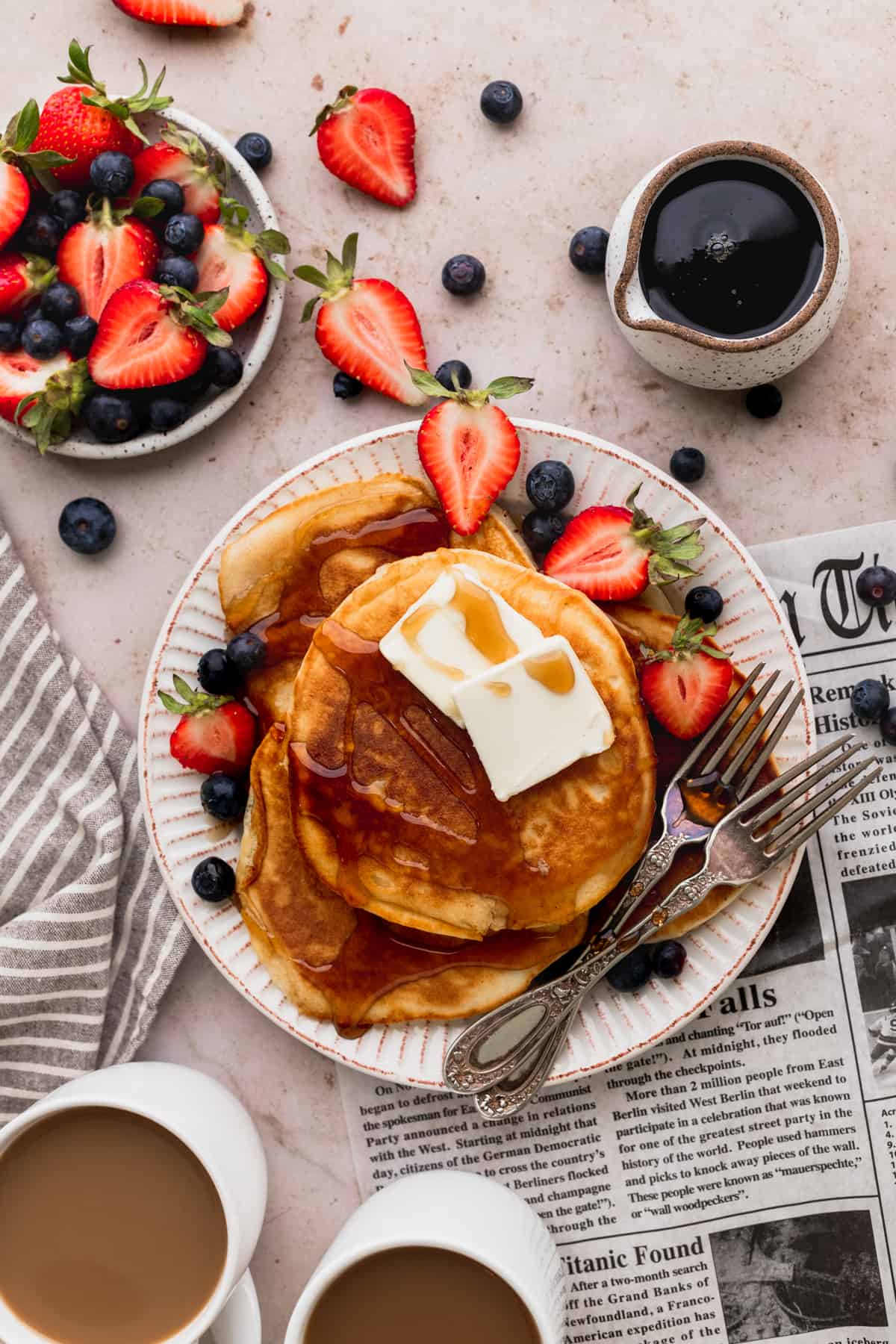 One plate of three pancakes with butter and syrup with fruit around it.