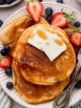 Close up of sweet cream pancakes on a large plate with strawberries and blueberries.