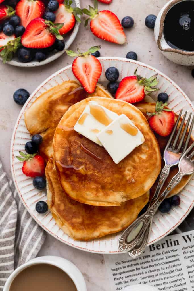 Close up of sweet cream pancakes on a large plate with strawberries and blueberries.