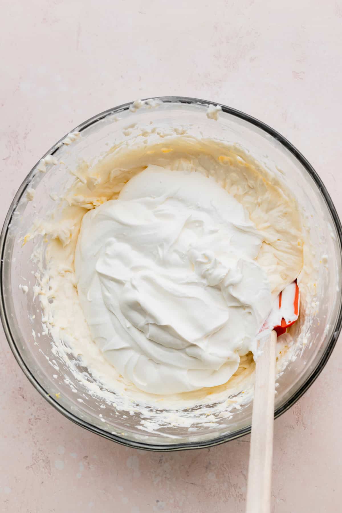 Whipped cream on top of cream cheese mixture in a glass bowl.