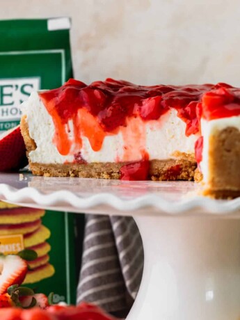 Lemon cheesecake with strawberry sauce cut into on a cake stand.