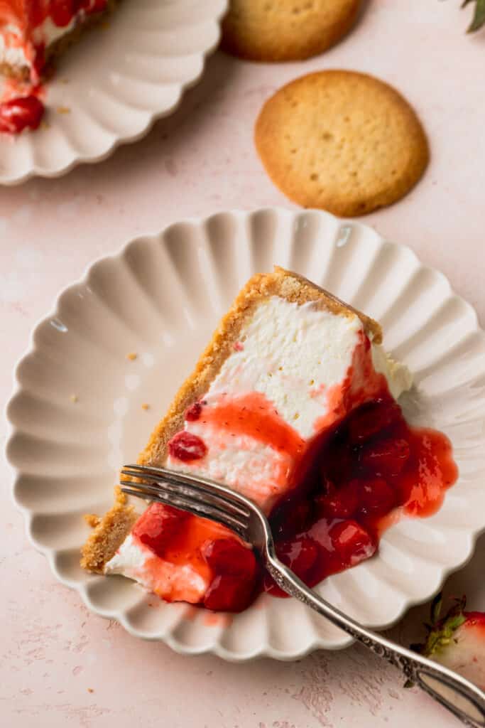 Slice of cheesecake on its side with a fork inserted on a plate.