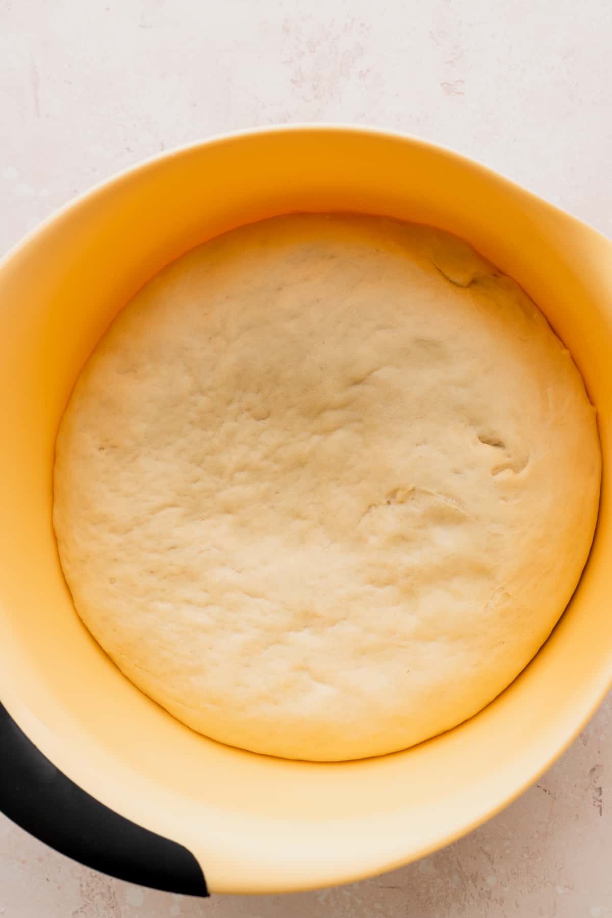Dough after rising in a yellow bowl.