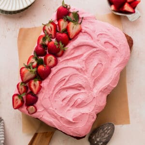 Strawberry sheet cake on a cutting board with strawberries on top.