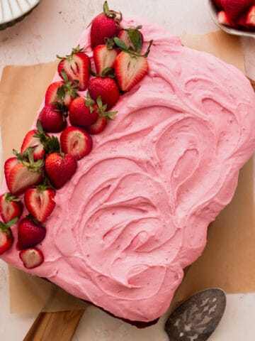 Strawberry sheet cake on a cutting board with strawberries on top.