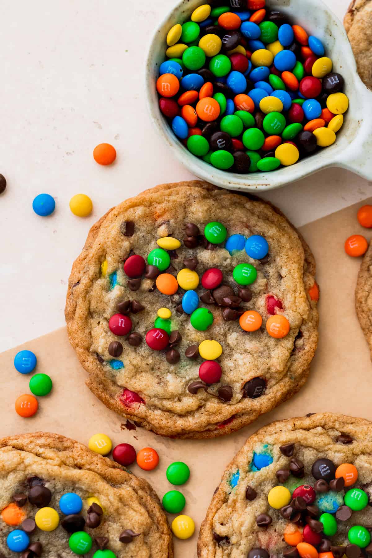 One cookie on parchment paper with a bowl of mini M&Ms.