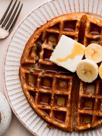 Banana waffles on a plate topped with butter, syrup, and bananas.