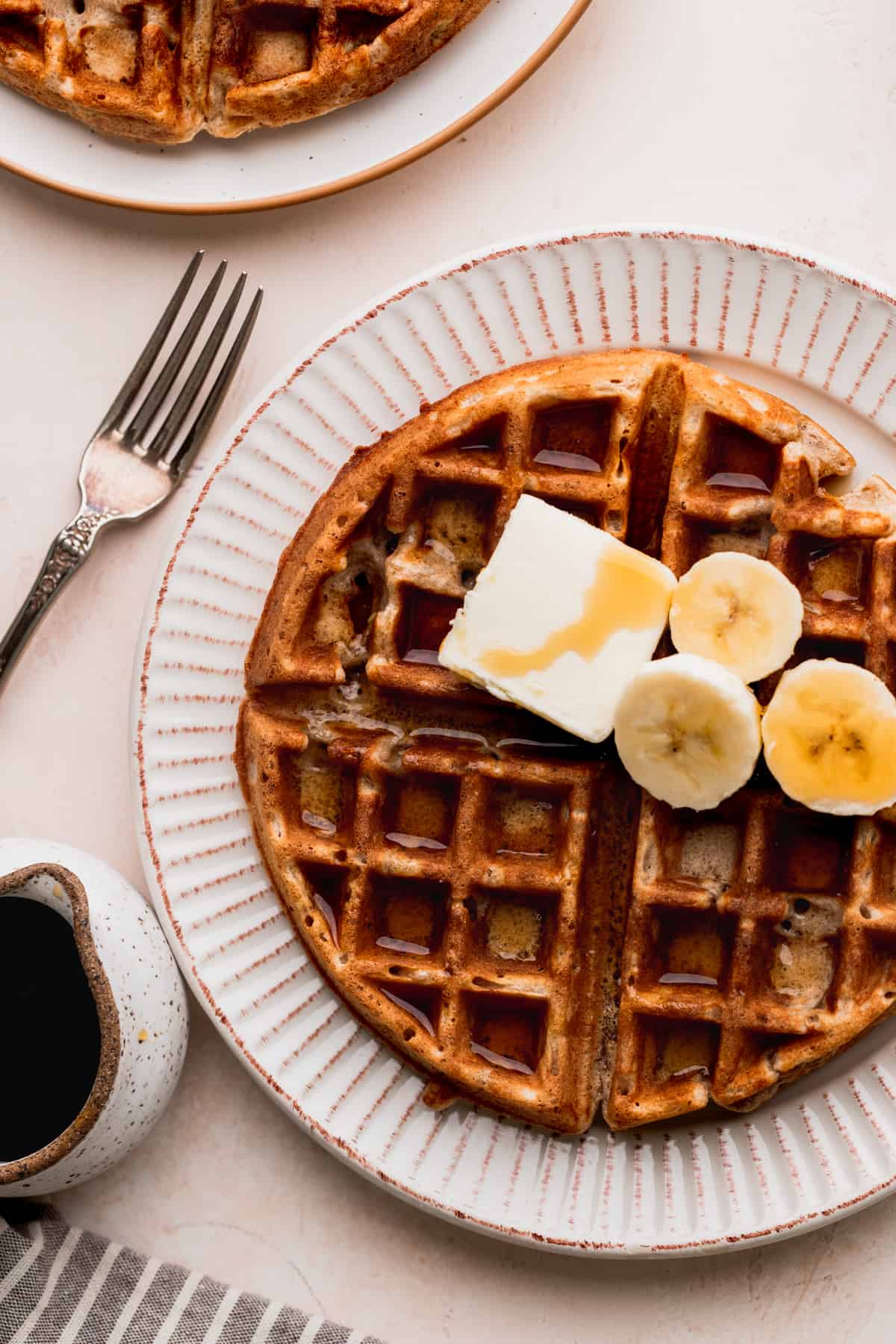 Banana waffles on a plate topped with butter, syrup, and bananas.