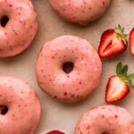 Close up of strawberry glazed donuts with strawberries on the side.