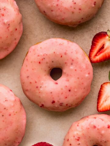 Close up of strawberry glazed donuts with strawberries on the side.