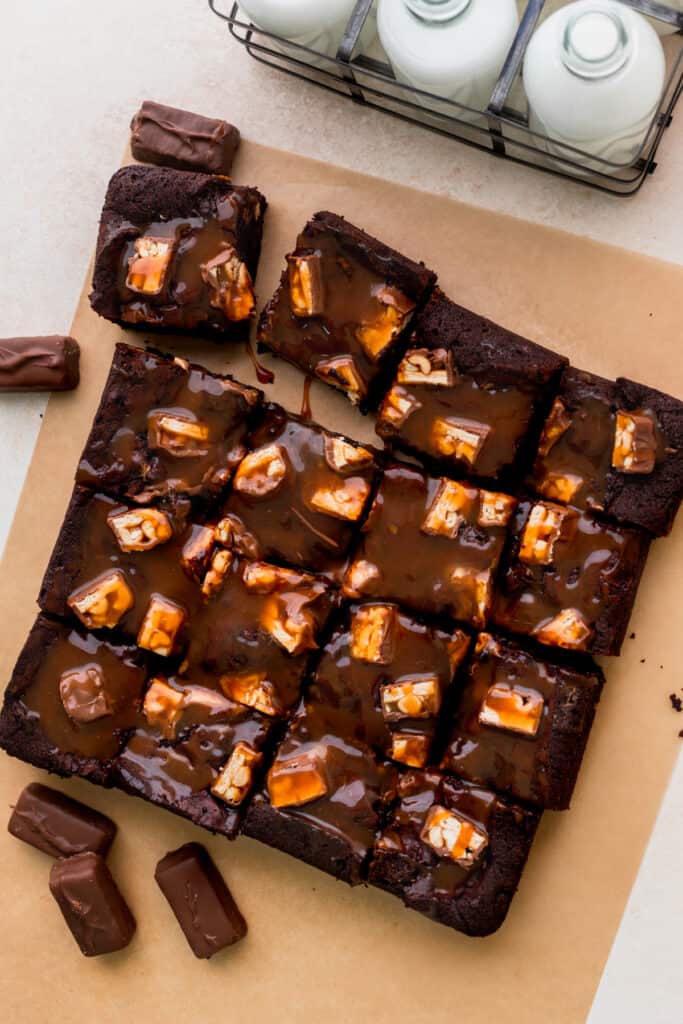 Snickers brownies cut up on parchment paper.