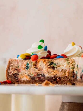 M&M cheesecake on a cake stand cut into.