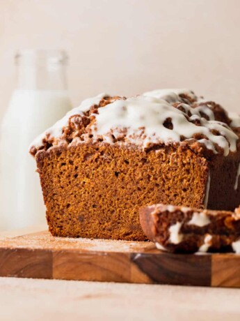 Pumpkin bread with cream cheese frosting on a wood board.