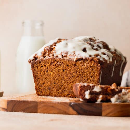Pumpkin bread with cream cheese frosting on a wood board.
