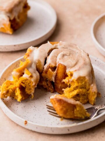 One pumpkin cinnamon roll on a plate with a bite missing.