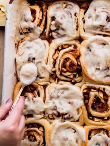 Spreading icing on top of the apple cinnamon rolls.