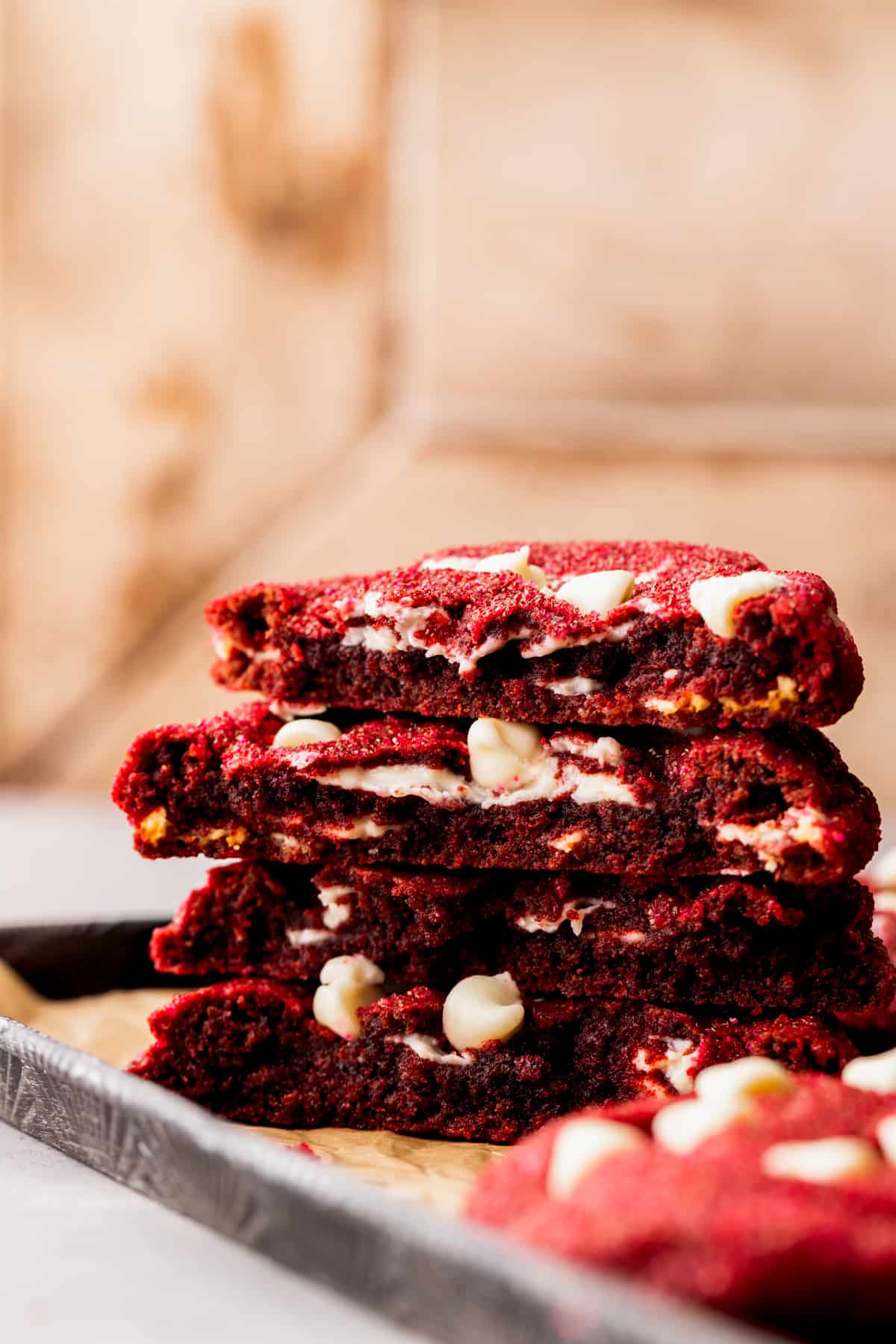 Two red velvet cookies split in half on a cookie sheet.