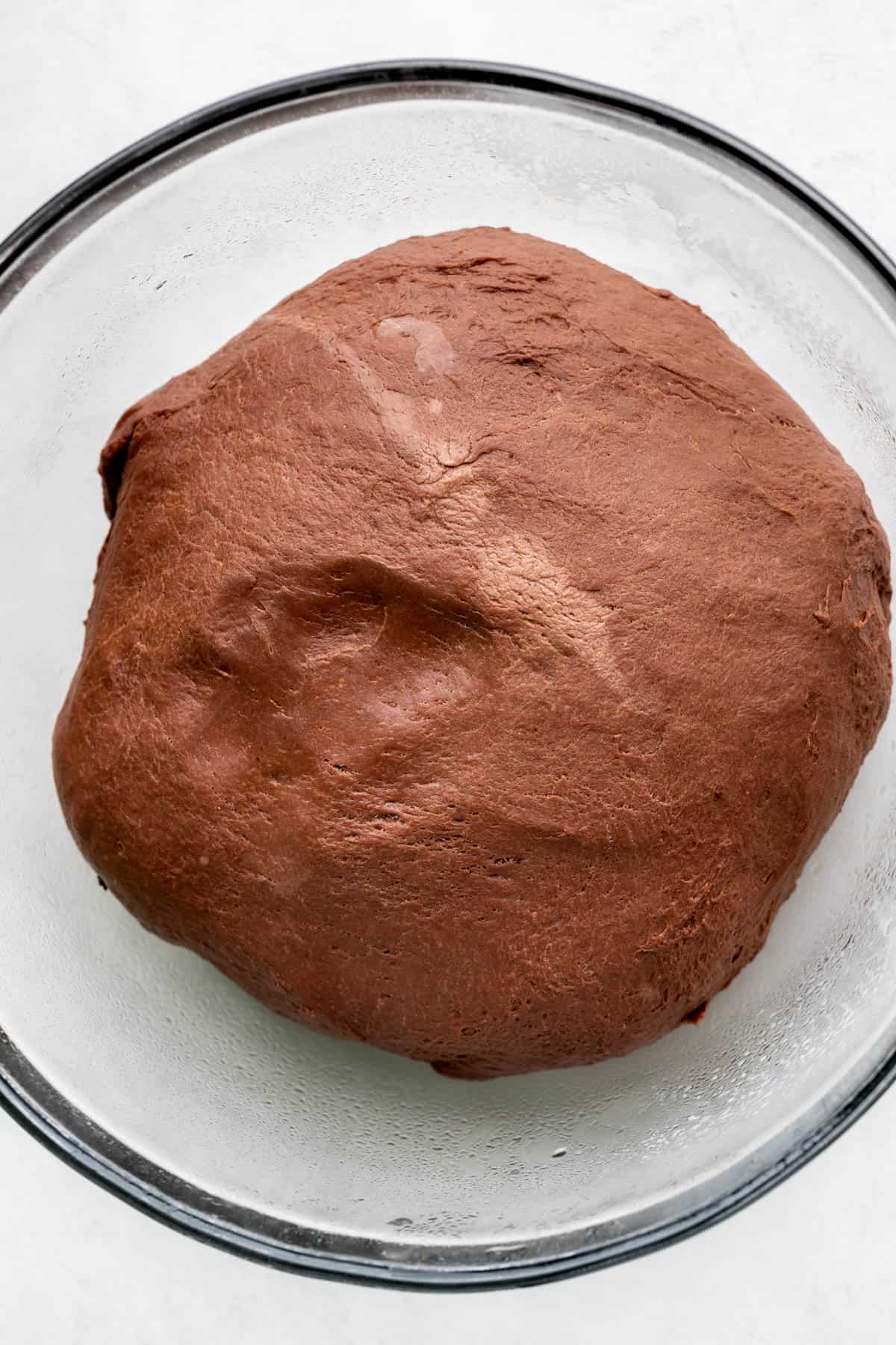 Raised chocolate dough in a glass bowl.