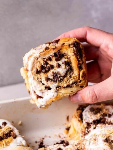Taking one cinnamon roll out of the pan.