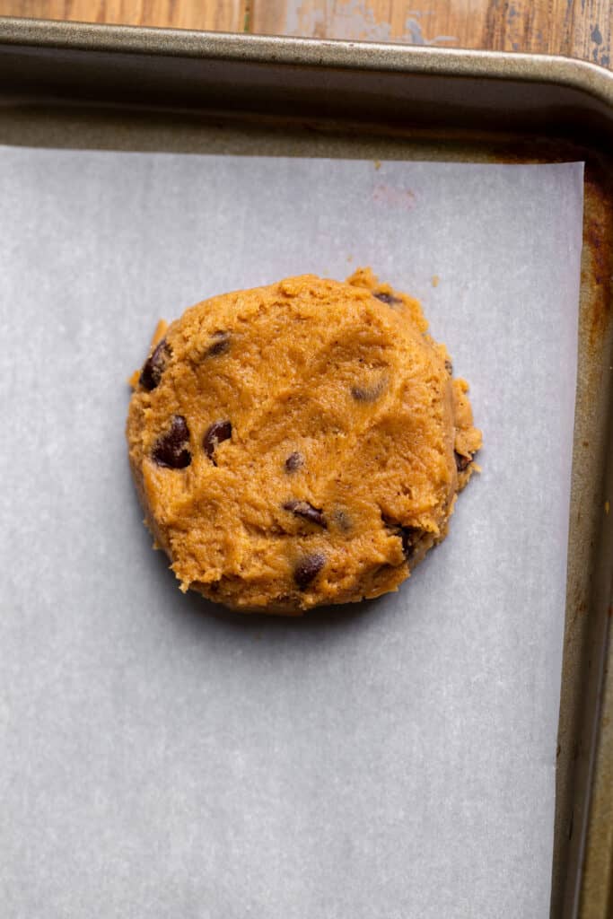 Cookie dough ball flattened on a cookie sheet.