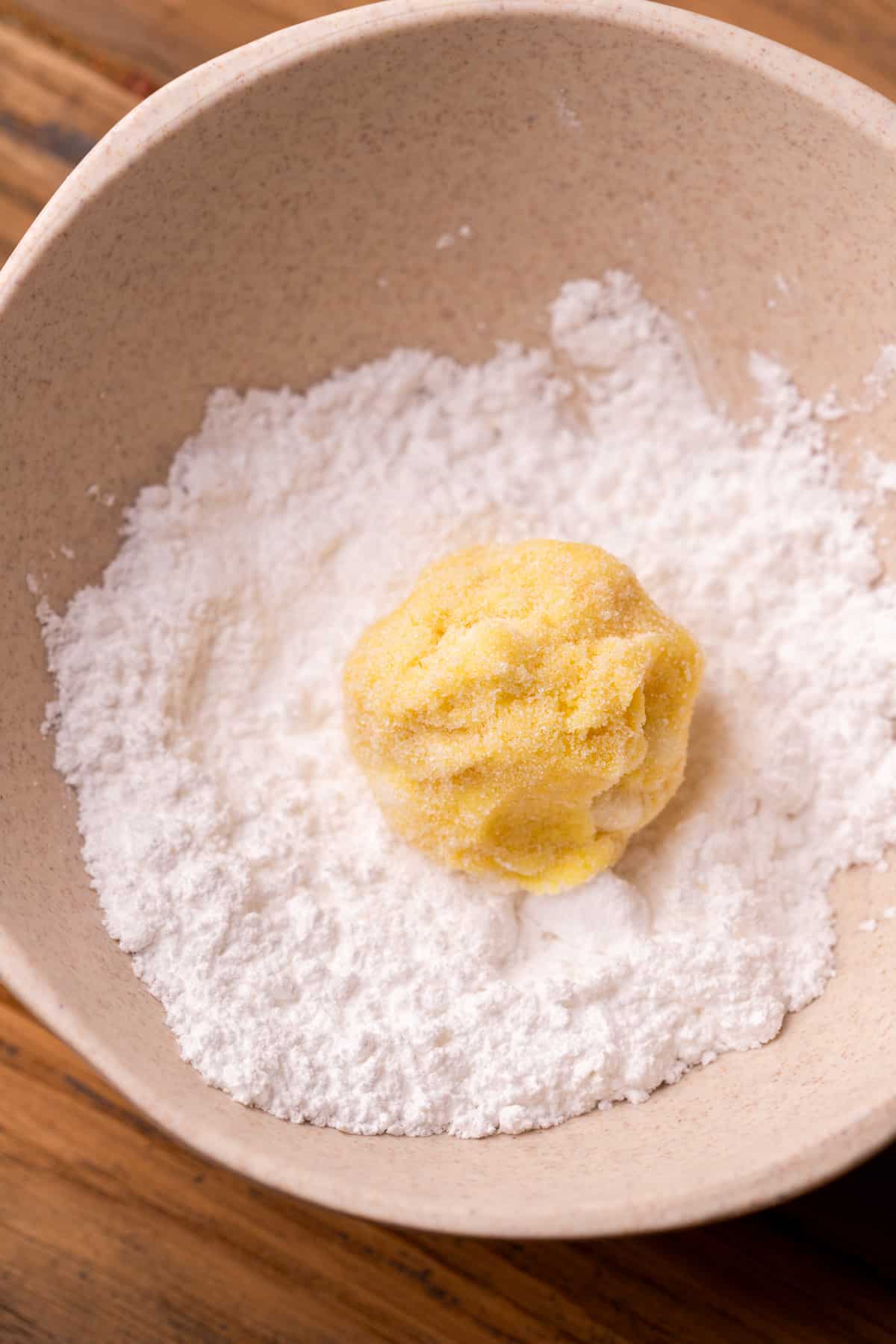 Cookie dough ball in a bowl of powdered sugar.