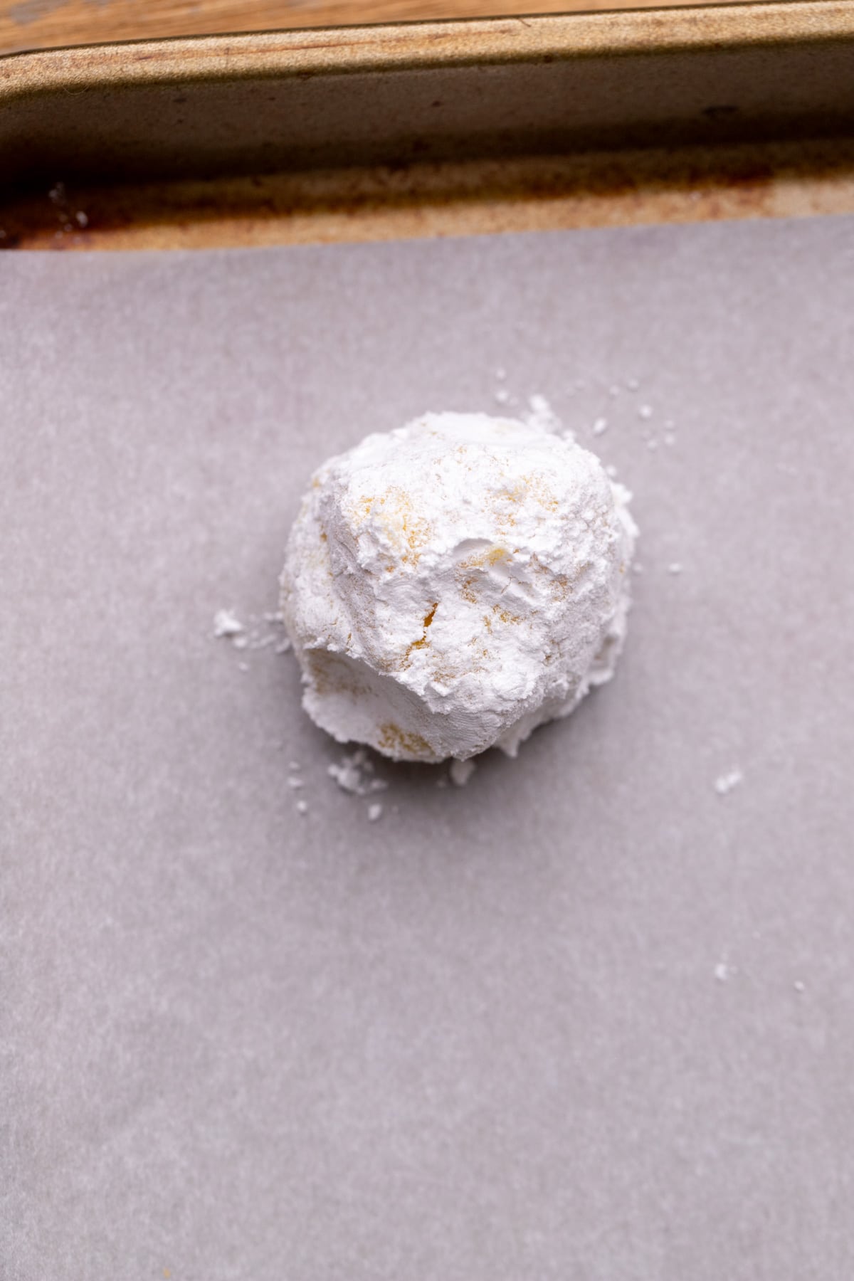 Cookie dough ball on cookie sheet covered in powdered sugar.