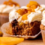 Bite missing from a peach cupcake.