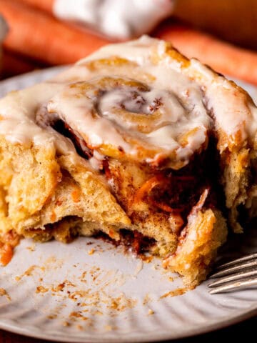 A bite missing from carrot cake cinnamon roll on a plate.
