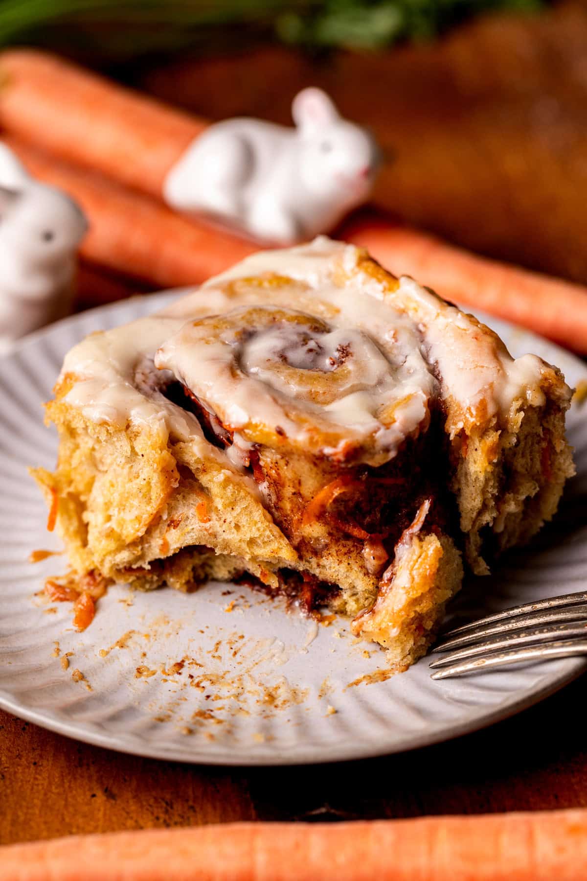A bite missing from carrot cake cinnamon roll on a plate.