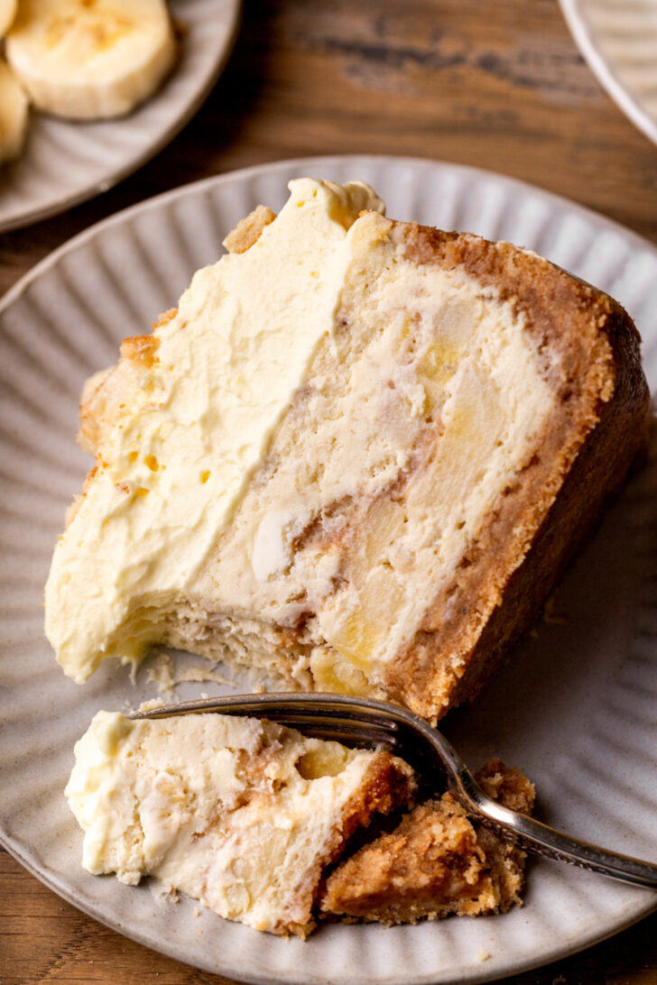 One slice of cheesecake on a plate with a bite missing.