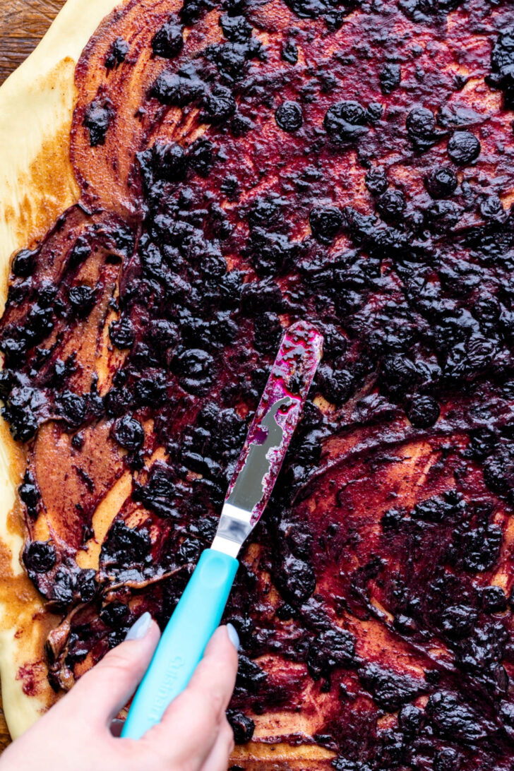 Spreading blueberry jam on top of dough.