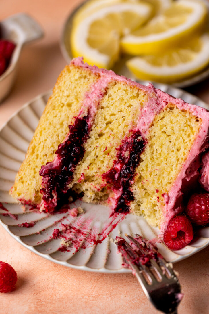 One slice of lemon raspberry cake on a plate with a bite missing.