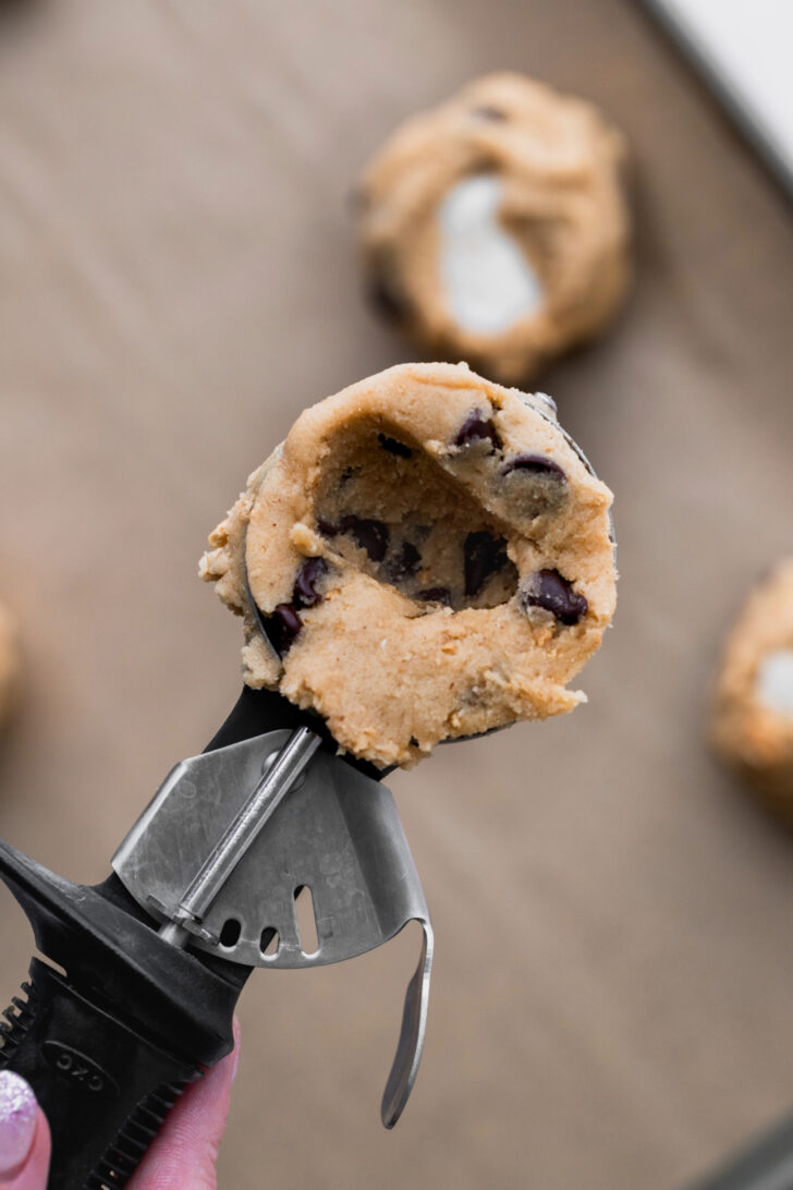 Cookie dough in a cookie scoop with hole pressed in.