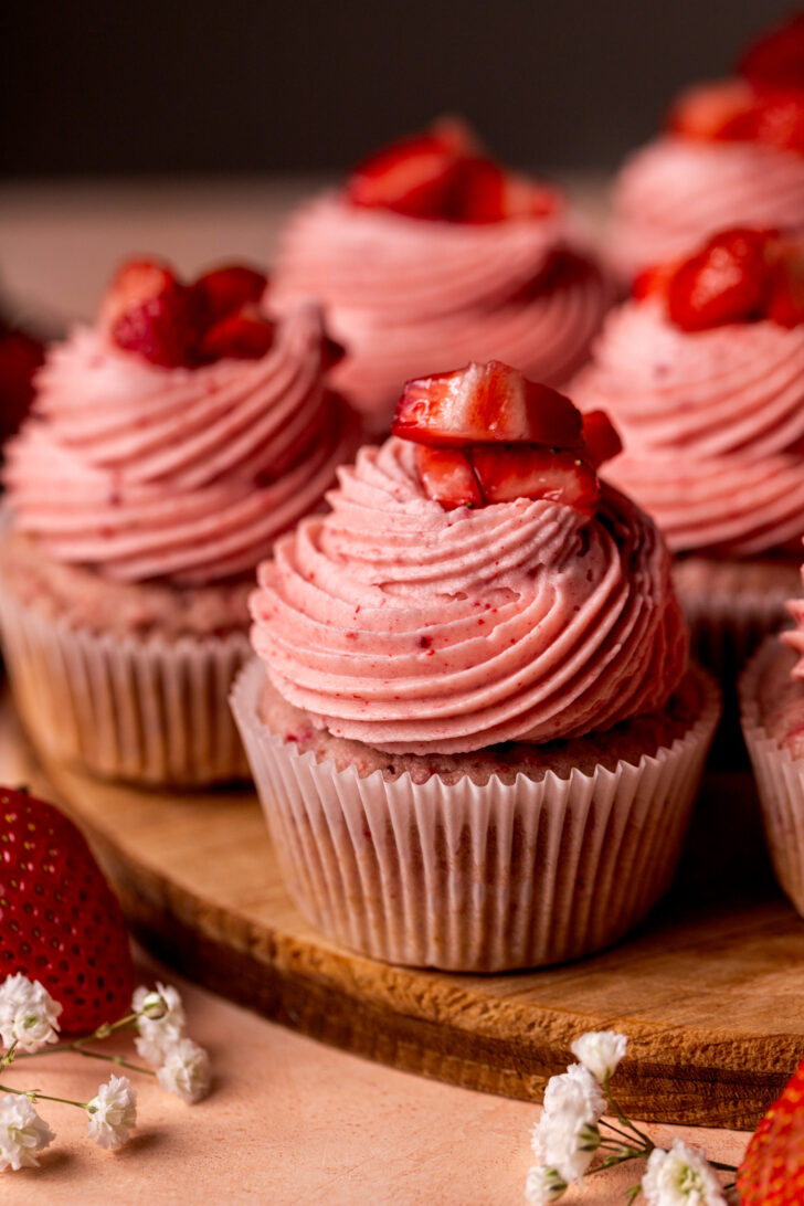 One strawberry cupcake on a wood board.