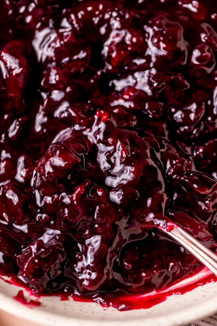 A spoon inserted into a bowl of cherry pie filling.
