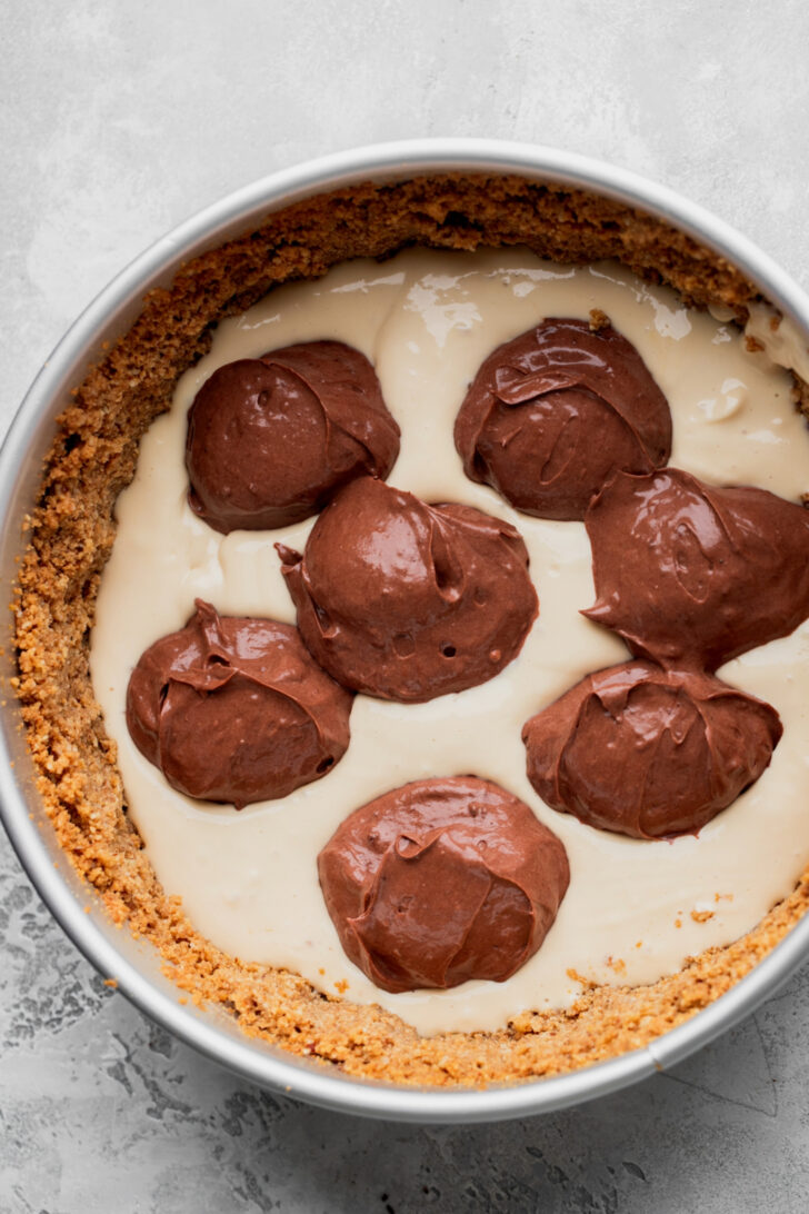 Chocolate cheesecake batter dolloped on top of crust.