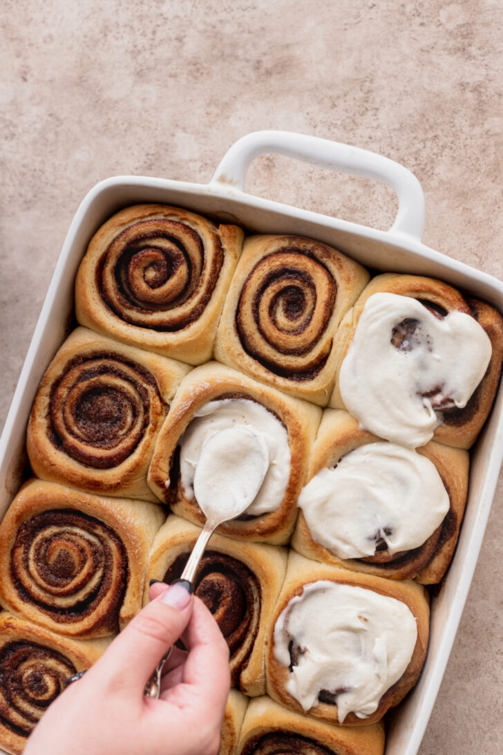 Spreading the icing on top of the rolls.