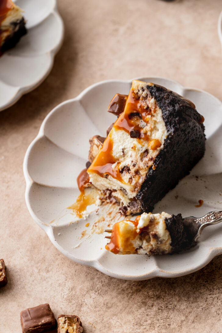 A slice of Snickers cheesecake on its side on a plate.