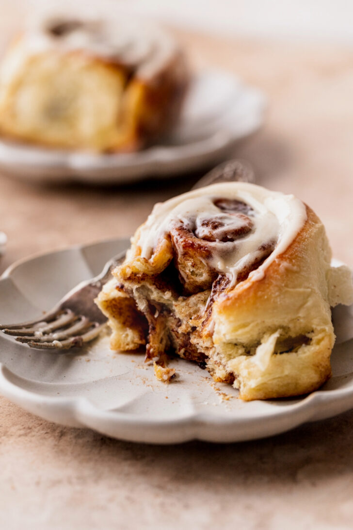 Bite missing from a homemade cinnamon roll on a plate.