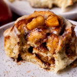 Bite missing from apple cinnamon rolls on a plate.