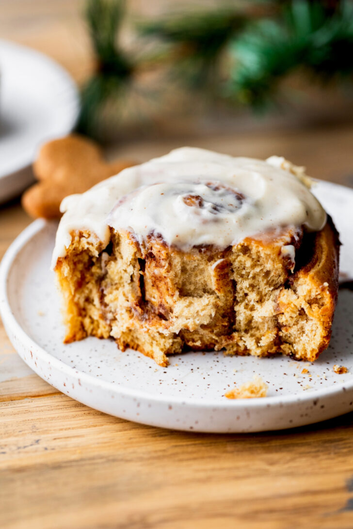One gingerbread cinnamon roll on a plate with a bite missing.