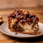One slice of pecan pie cheesecake on a plate.
