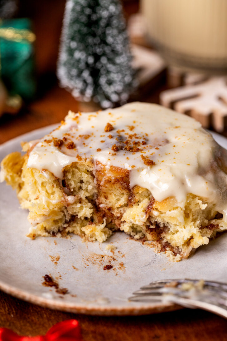 One cinnamon rolls with a bite missing on a plate.