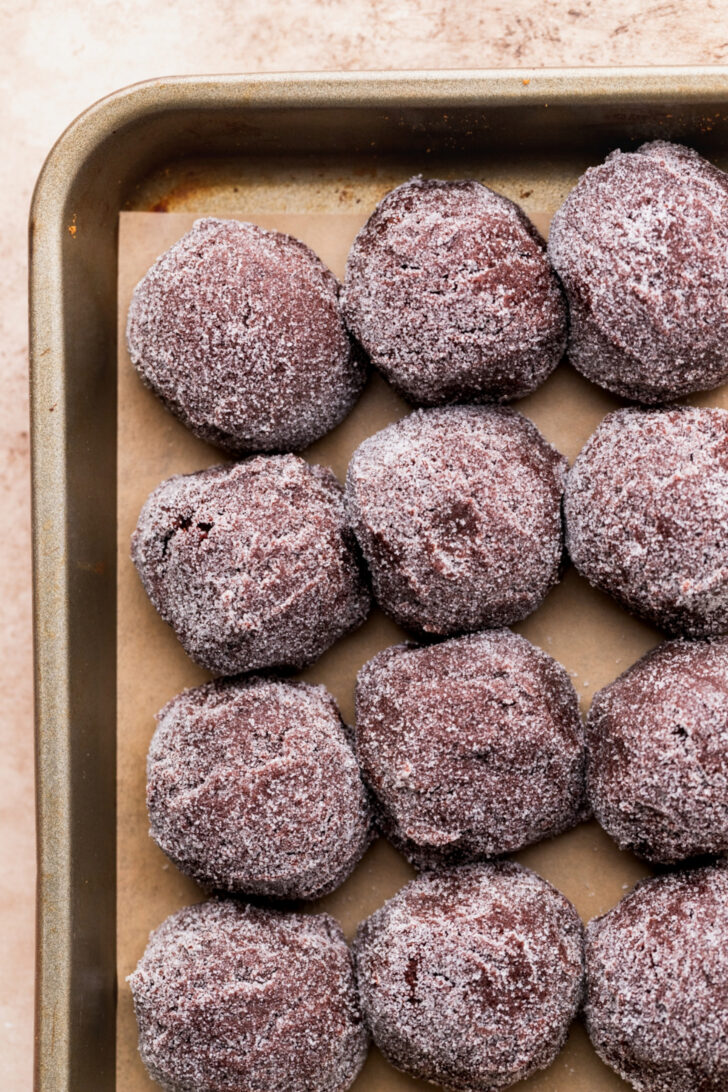 Cookie dough balls rolled in sugar on cookie sheet.