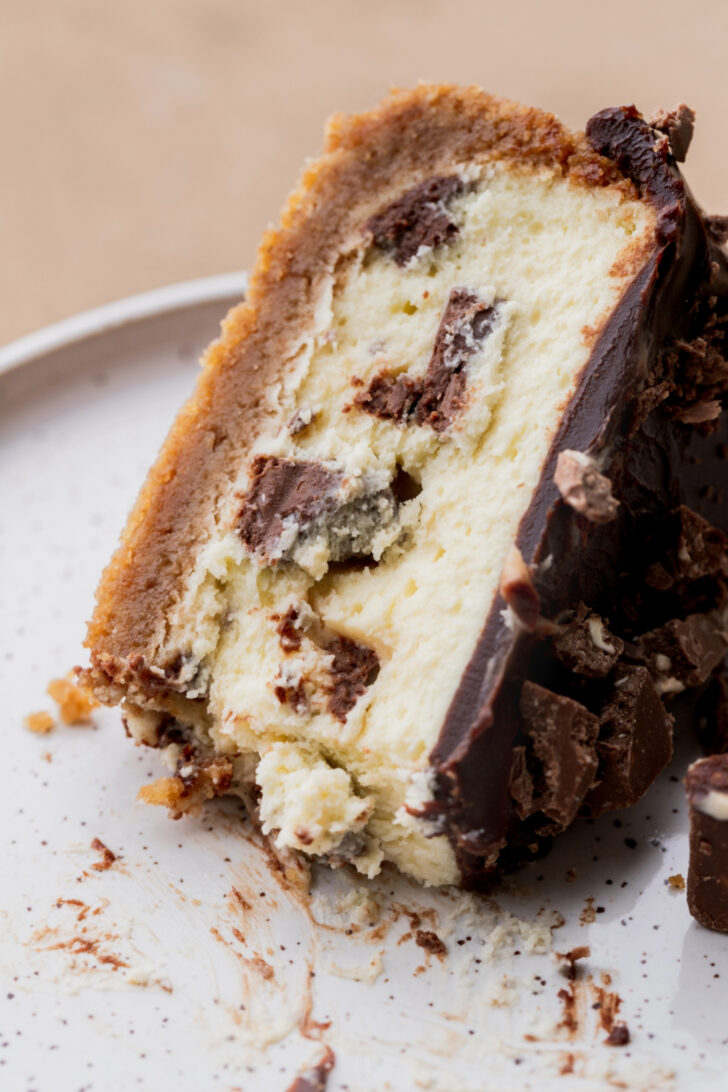 One slice of cheesecake with a bite missing on a plate.